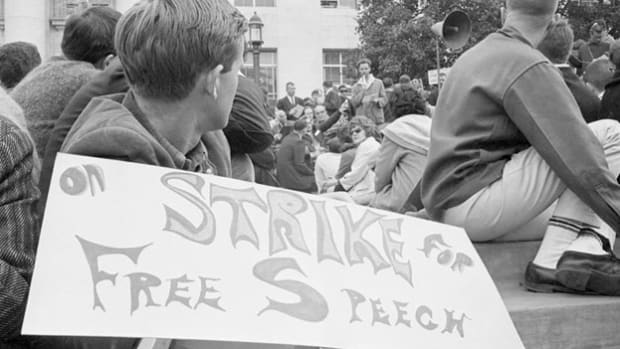 The first major U.S. campus uprising of the 1960s occurred on October 1, 1964, at the University of California at Berkeley. That day, Jack Weinberg, a Congress of Racial Equality student activist, was arrested for handing out leaflets on campus in defiance of a campus ban on political activity. Police put Weinberg in a squad car, but before it could drive away thousands of student surrounded the vehicle, keeping it immobile for the next 32 hours and making speeches from its roof. The protest marked the beginning of the Free Speech Movement, a series of demonstrations at UC-Berkeley that culminated on December 2, 1964, when 1,200 students took over Sproul Hall on campus, demanding an end to speech restrictions. At the Sproul protest, folk singer Joan Baez sang ''We Shall Overcome'' and Free Speech leader Mario Savio declared, ''There comes a time when the operation of the machine becomes so odious, makes you so sick at heart, that you can't take part, you can't even passively take part. And you've got to put your bodies on the gears, and upon the wheels, upon the levers, upon all the apparatus. And you've got to make it stop.'' California state troopers were called in to break up the sit-in, and they arrested 800 students, dozens of whom were injured by the police. A student strike then shut down the campus until the faculty senate voted to support the students' Free Speech Movement, compelling the administration to lift political restrictions. UC-Berkeley would remain a hotbed of political protest throughout the 1960s, and antiwar and civil rights protesters would employ many of the methods developed by the Free Speech Movement activists.
