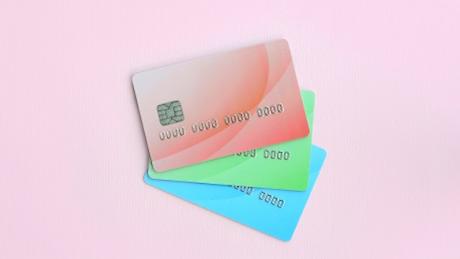 Three colored credit cards lay on a pastel pink background. The concept of a variety of banking services and types of bank card applications