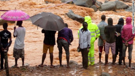 Bystanders look on as floodwaters rage past a damaged building in an area of Freetown on August 14, 2017, after landslides struck the capital of the west African state of Sierra Leone.               
At least 312 people were killed and more than 2,000 left homeless when heavy flooding hit Sierra Leone&#39;s capital of Freetown, leaving morgues overflowing and residents desperately searching for loved ones. An AFP journalist at the scene saw bodies being carried away and houses submerged in two areas of the city, where roads turned into churning rivers of mud and corpses were washed up on the streets.
 / AFP PHOTO / SAIDU BAH        (Photo credit should read SAIDU BAH/AFP/Getty Images)