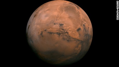 Mosaic of the Valles Marineris hemisphere of Mars projected into point perspective, a view similar to that which one would see from a spacecraft. The distance is 2500 kilometers from the surface of the planet, with the scale being .6km/pixel. The mosaic is composed of 102 Viking Orbiter images of Mars. The center of the scene (lat -8, long 78) shows the entire Valles Marineris canyon system, over 2000 kilometers long and up to 8 kilometers deep, extending form Noctis Labyrinthus, the arcuate system of graben to the west, to the chaotic terrain to the east. Many huge ancient river channels begin from the chaotic terrain from north-central canyons and run north. The three Tharsis volcanoes (dark red spots), each about 25 kilometers high, are visible to the west. South of Valles Marineris is very ancient terrain covered by many impact craters. 